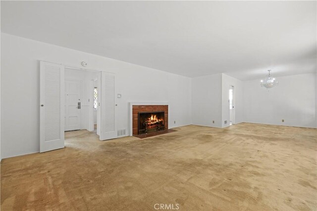 unfurnished living room featuring a brick fireplace, carpet, and an inviting chandelier