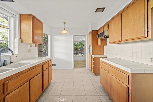 kitchen featuring tile countertops, tasteful backsplash, light tile patterned flooring, hanging light fixtures, and sink