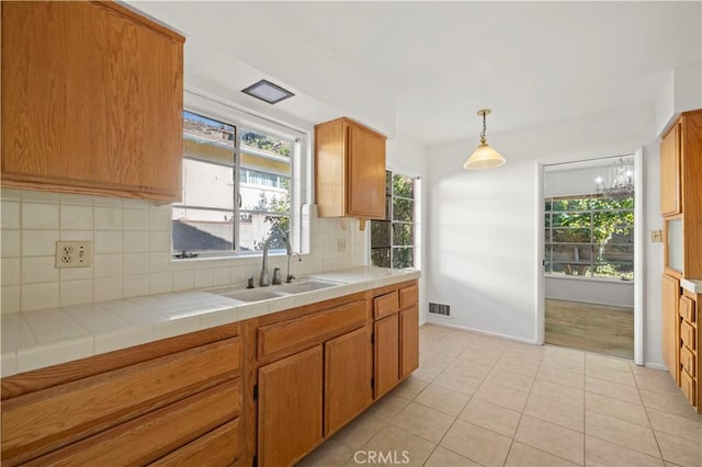 kitchen featuring tasteful backsplash, sink, hanging light fixtures, tile counters, and light tile patterned floors