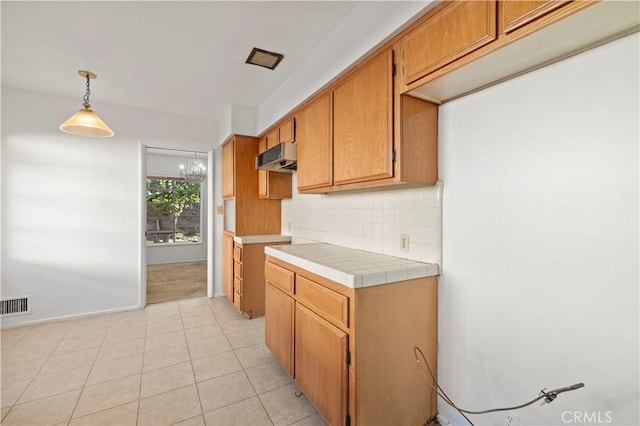 kitchen with white fridge, pendant lighting, decorative backsplash, tile counters, and a chandelier