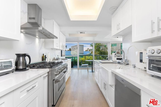 kitchen with white cabinetry, light stone counters, wall chimney range hood, and appliances with stainless steel finishes