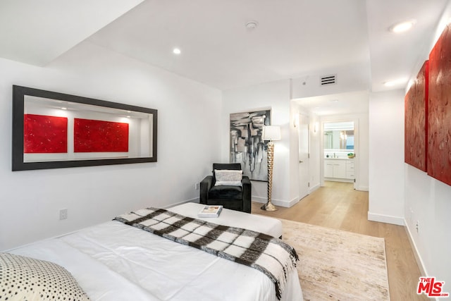 bedroom featuring a closet, connected bathroom, and light hardwood / wood-style flooring