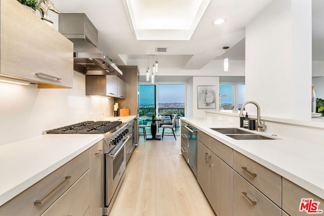 kitchen featuring stainless steel appliances, decorative light fixtures, light wood-type flooring, wall chimney range hood, and sink