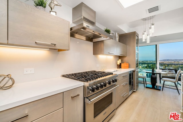 kitchen with pendant lighting, high end range, beverage cooler, wall chimney range hood, and light hardwood / wood-style flooring