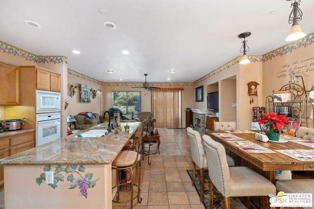 kitchen featuring pendant lighting, white appliances, light brown cabinetry, sink, and ceiling fan