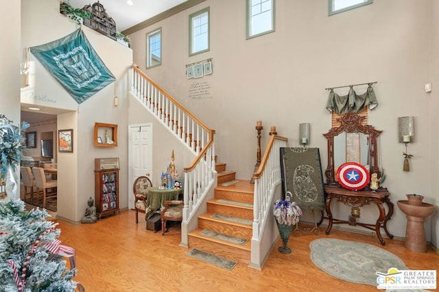 stairs with a high ceiling, hardwood / wood-style floors, crown molding, and a healthy amount of sunlight