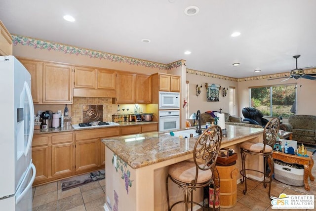 kitchen with a center island with sink, ceiling fan, white appliances, a kitchen breakfast bar, and sink