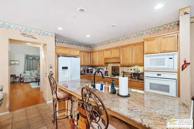 kitchen with light stone countertops, white appliances, light brown cabinetry, a kitchen breakfast bar, and light tile patterned floors