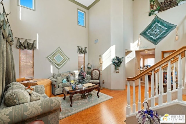 living room featuring light hardwood / wood-style flooring, crown molding, and a towering ceiling