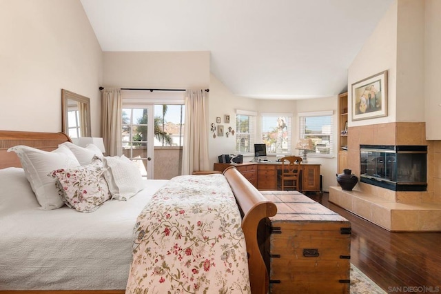 bedroom with lofted ceiling, a tiled fireplace, multiple windows, and hardwood / wood-style floors