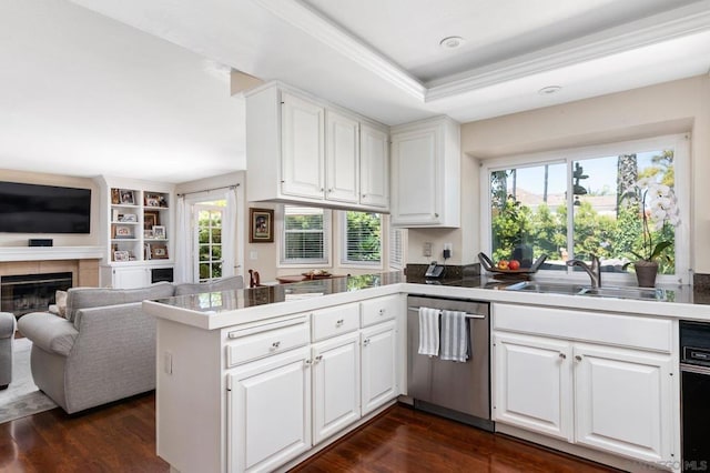 kitchen featuring white cabinets, a fireplace, a raised ceiling, kitchen peninsula, and stainless steel dishwasher