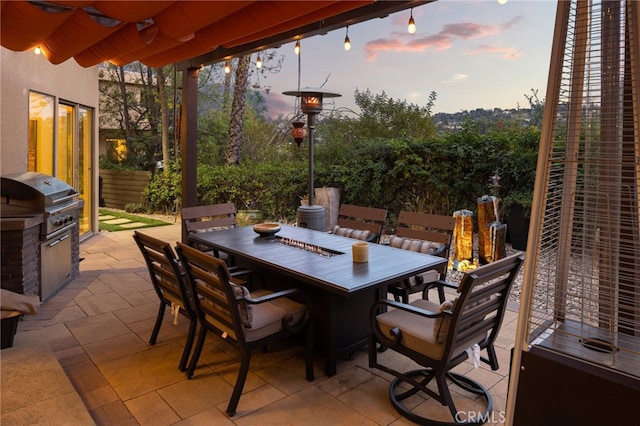 patio terrace at dusk featuring outdoor dining space, grilling area, and exterior kitchen