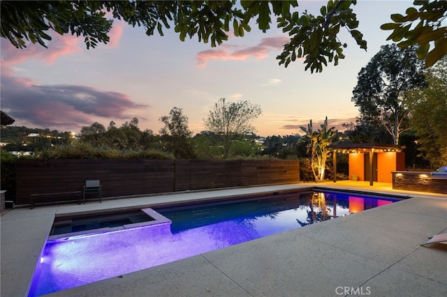 pool at dusk featuring a fenced backyard, a pool with connected hot tub, and a patio