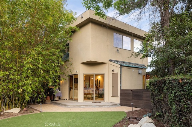 rear view of property featuring a patio, stucco siding, a standing seam roof, metal roof, and fence