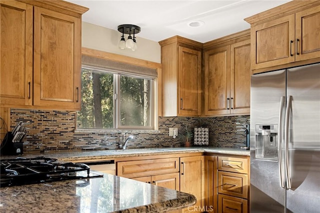 kitchen featuring decorative backsplash, light stone countertops, stainless steel fridge, and black gas stovetop