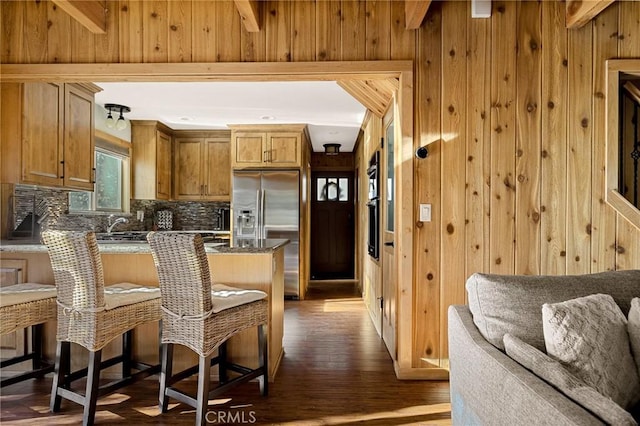 kitchen featuring backsplash, wood walls, beam ceiling, dark wood-type flooring, and stainless steel fridge