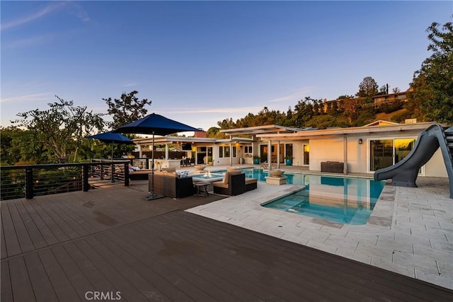 pool at dusk featuring a deck, a water slide, a jacuzzi, and an outdoor pool