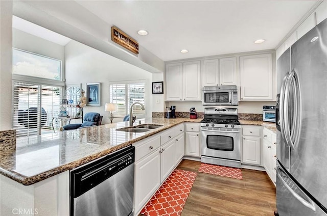 kitchen with kitchen peninsula, stainless steel appliances, dark stone countertops, white cabinets, and sink