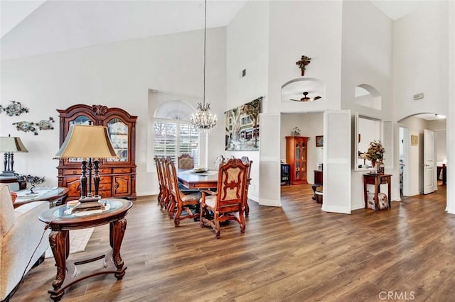 dining area with high vaulted ceiling, dark wood-type flooring, and ceiling fan with notable chandelier