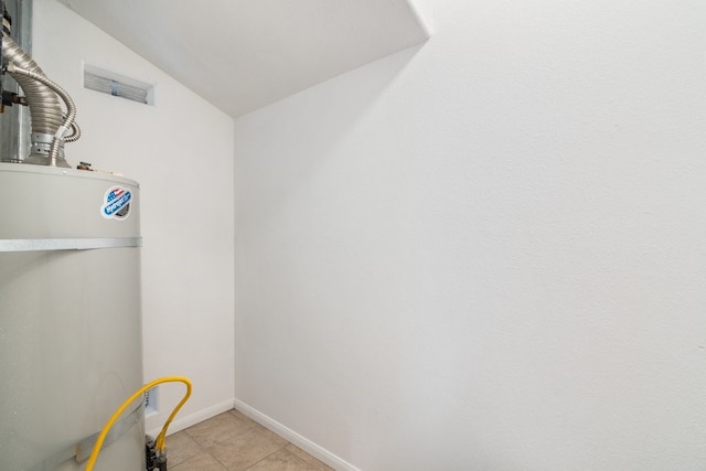 clothes washing area featuring light tile patterned floors and water heater