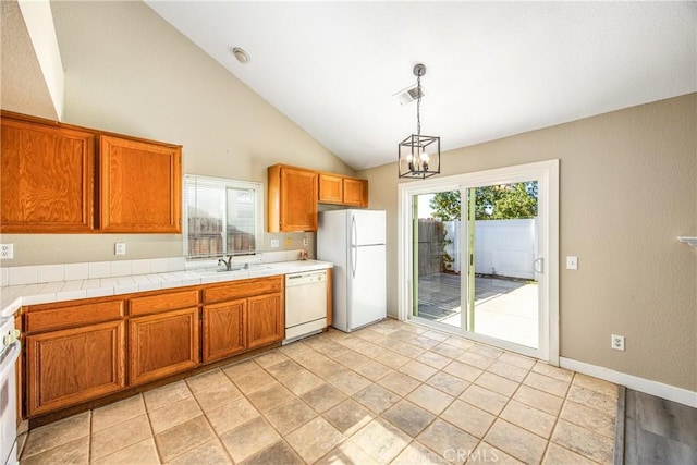 kitchen featuring sink, white appliances, hanging light fixtures, tile counters, and vaulted ceiling