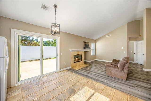 unfurnished living room featuring a tiled fireplace, high vaulted ceiling, a chandelier, and light wood-type flooring