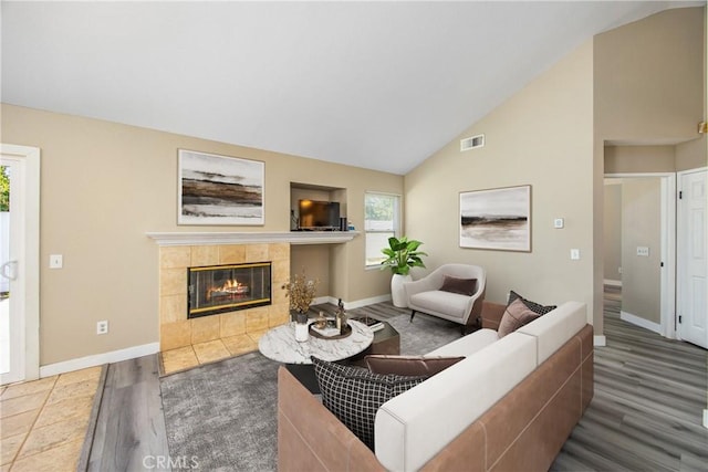 living room with a healthy amount of sunlight, dark hardwood / wood-style flooring, a tiled fireplace, and high vaulted ceiling