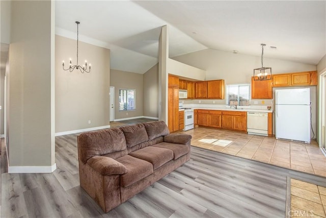 living room with high vaulted ceiling, sink, an inviting chandelier, and light hardwood / wood-style flooring