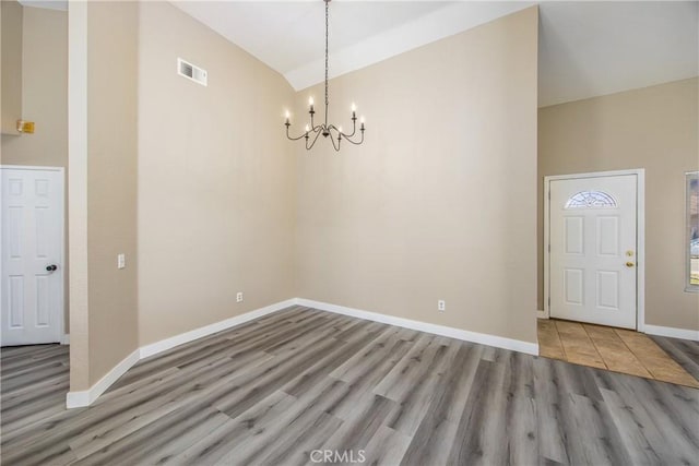 unfurnished dining area with lofted ceiling, a notable chandelier, and light hardwood / wood-style flooring