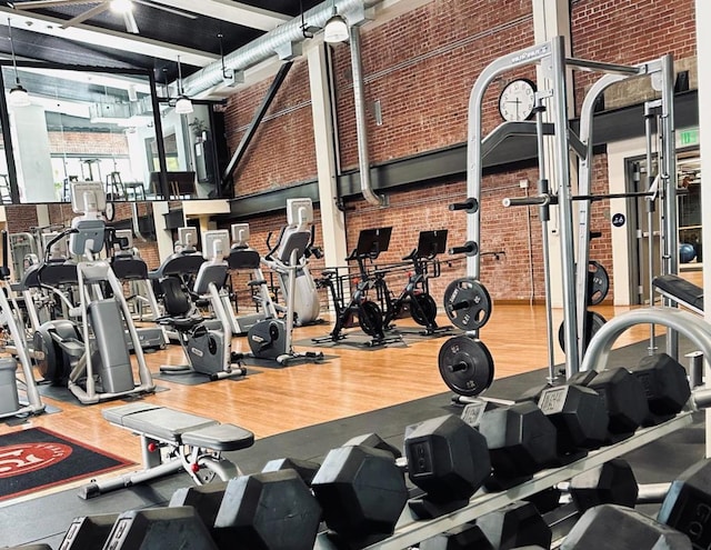 gym featuring brick wall, a towering ceiling, and wood-type flooring