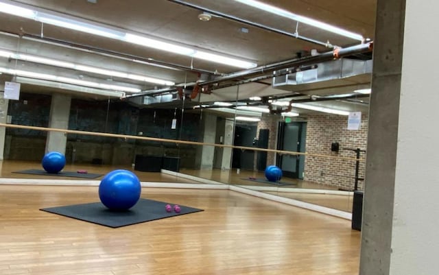 workout room with brick wall, wood-type flooring, and a towering ceiling