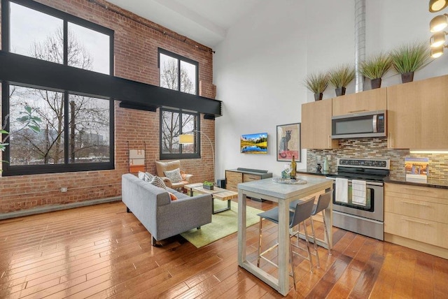 kitchen with brick wall, appliances with stainless steel finishes, light brown cabinets, and a high ceiling