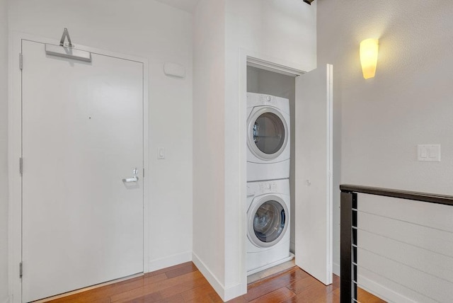 clothes washing area with wood-type flooring and stacked washer / drying machine