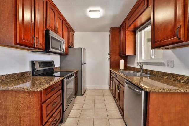 kitchen with light tile patterned flooring, appliances with stainless steel finishes, dark stone countertops, and sink