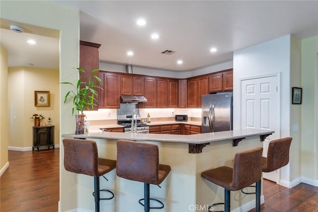 kitchen with dark wood-type flooring, a breakfast bar, appliances with stainless steel finishes, and kitchen peninsula