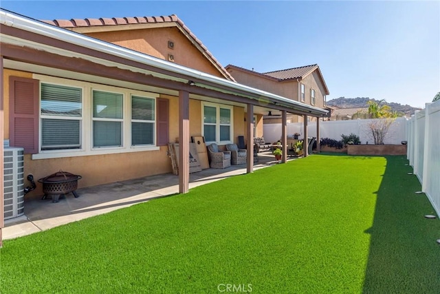 back of property with a fire pit, a yard, a fenced backyard, and a patio