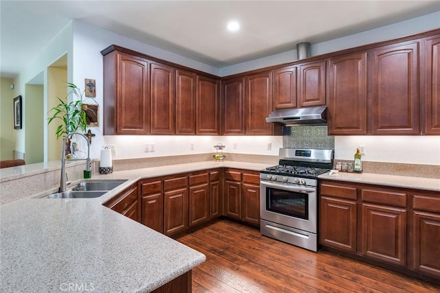 kitchen featuring a sink, dark wood finished floors, under cabinet range hood, light countertops, and stainless steel gas range