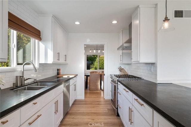 kitchen featuring stainless steel appliances, wall chimney exhaust hood, pendant lighting, white cabinets, and sink