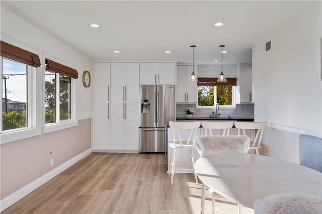 kitchen with white cabinets, sink, backsplash, hanging light fixtures, and stainless steel fridge