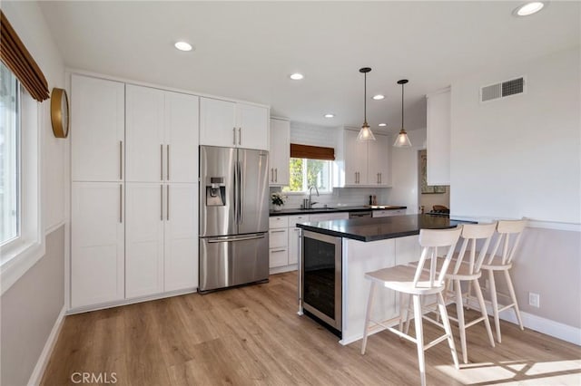 kitchen with a kitchen bar, stainless steel refrigerator with ice dispenser, decorative light fixtures, wine cooler, and white cabinets