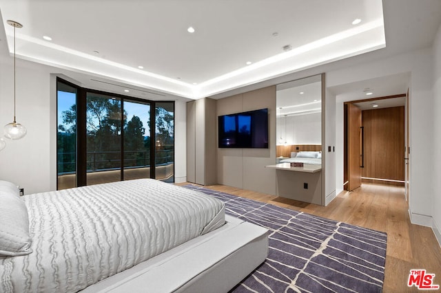 bedroom featuring light wood-type flooring, expansive windows, and a tray ceiling