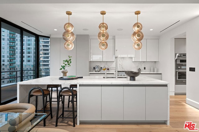 kitchen with white cabinetry, tasteful backsplash, light stone counters, and an island with sink