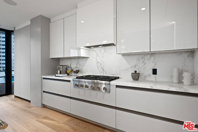 kitchen with backsplash, light hardwood / wood-style floors, stainless steel gas cooktop, light stone countertops, and white cabinets