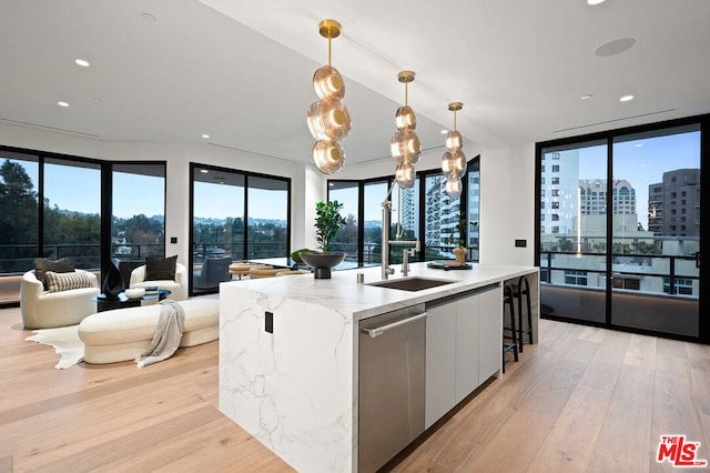 kitchen featuring an island with sink, white cabinets, hanging light fixtures, stainless steel dishwasher, and light stone counters