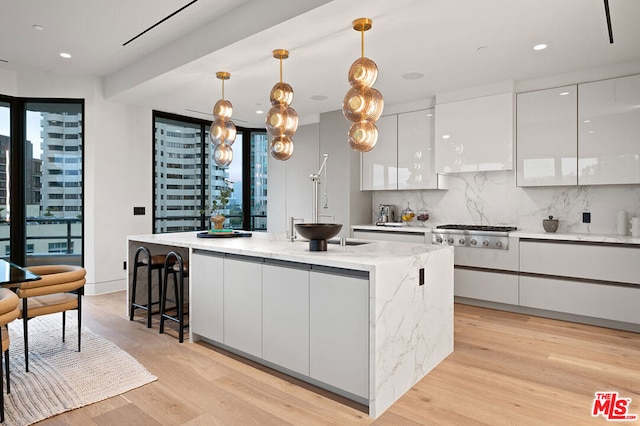 kitchen featuring light hardwood / wood-style floors, an island with sink, backsplash, decorative light fixtures, and white cabinets