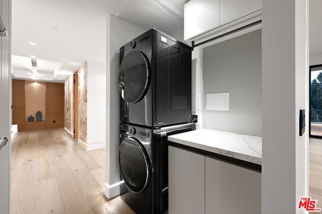 laundry area with stacked washer and clothes dryer and light hardwood / wood-style flooring