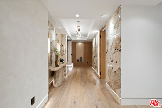 hallway with light wood-type flooring and a tray ceiling