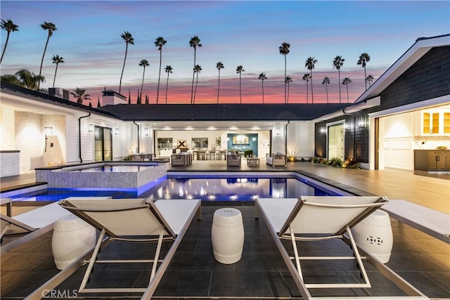 pool at dusk featuring a patio area and an in ground hot tub