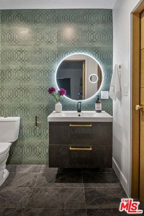 bathroom featuring toilet, vanity, and tile walls