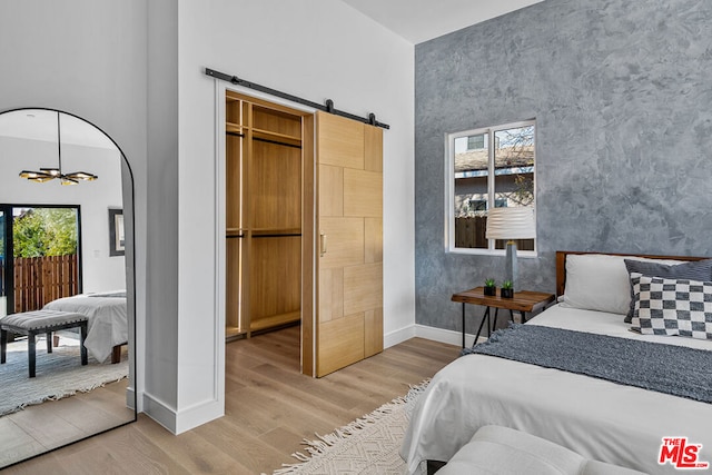 bedroom with a barn door, wood-type flooring, a high ceiling, an inviting chandelier, and a closet